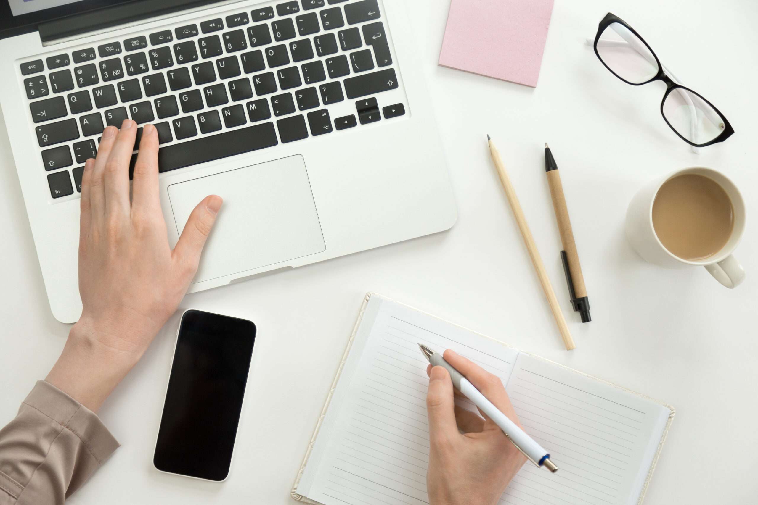 Hand working on a laptop, another holding a pen ready to write in the notebook. Business concept, high angle